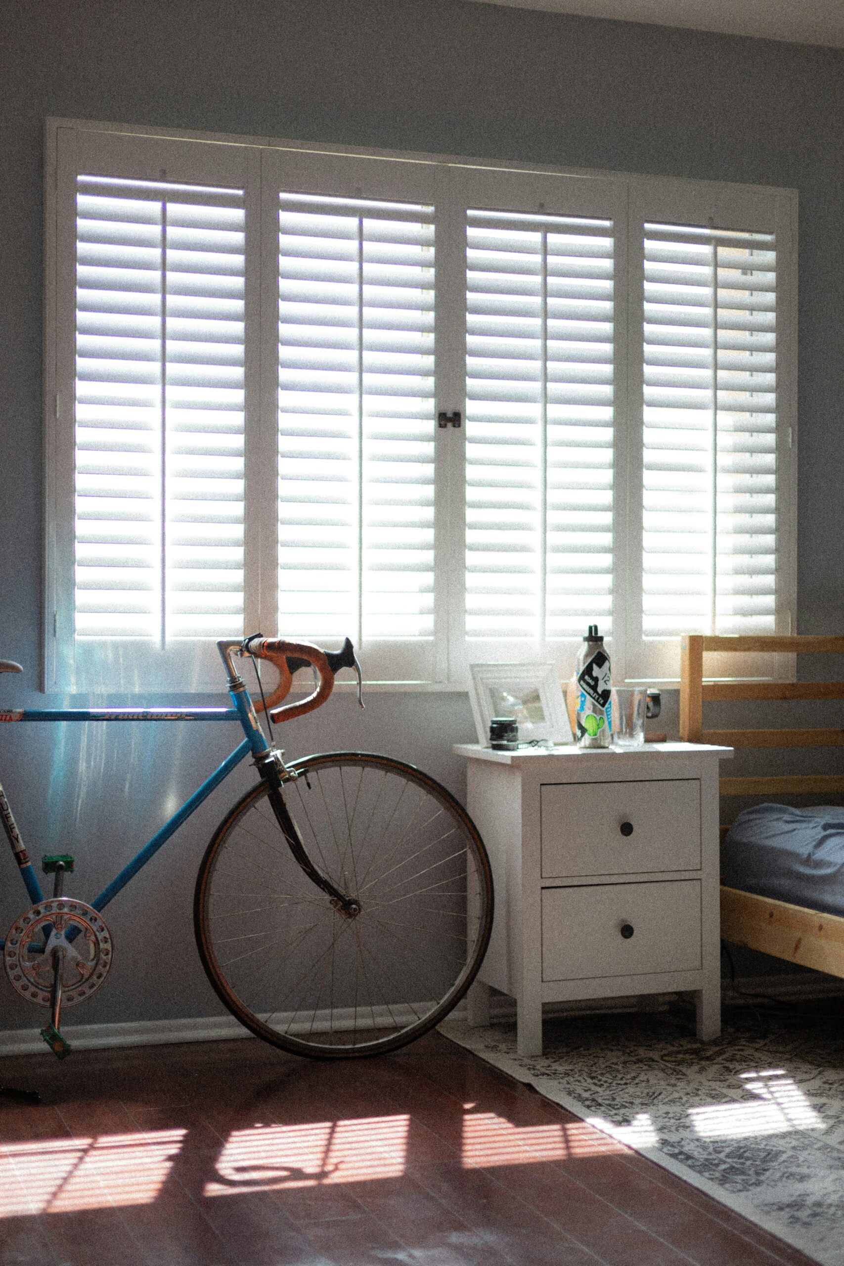 White plantation shutters installed on a bedroom window, providing privacy and filtered light. A bicycle rests against the window