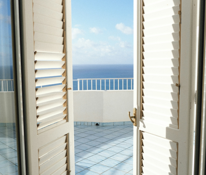 White french doors leading out to a sunny balcony with blue sky