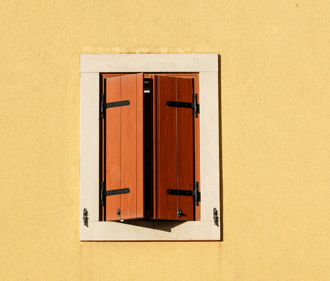 Solid brown wooden shutters in a painted yellow wall