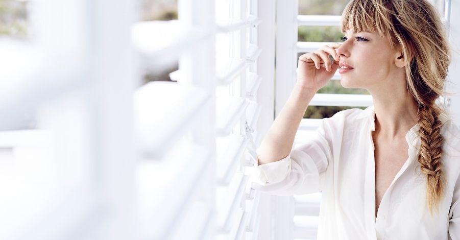 Sales on Shutters A white woman with plaited blond hair leaning against a shuttered window and looking outside